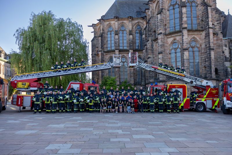 Großes Gruppenfoto der Feuerwehrleute in Einsatzkleidung vor einem historischen Gebäude mit zwei ausgefahrenen Drehleitern